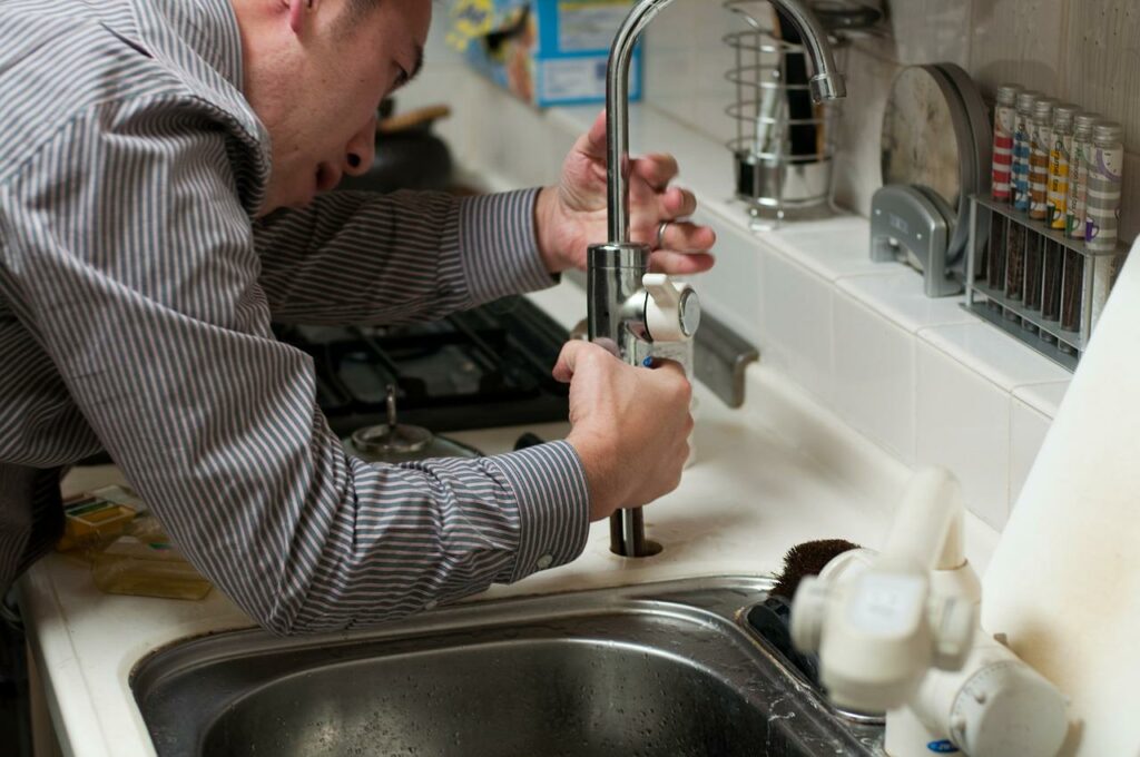 plumber fixing faucet in kitchen