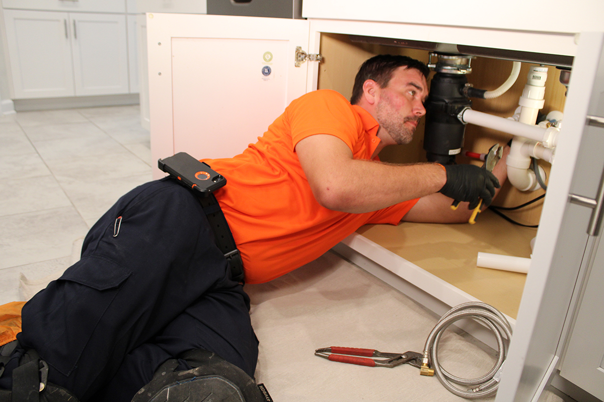 plumber in orange shirt fixing kitchen sink