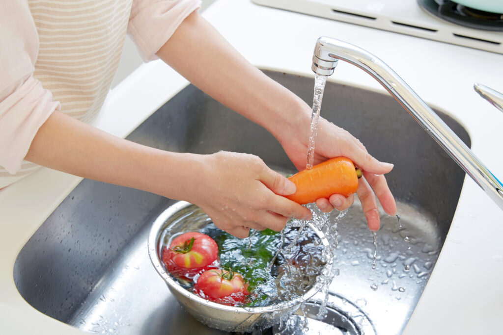 Woman's arms washing vegetables in a metal sink