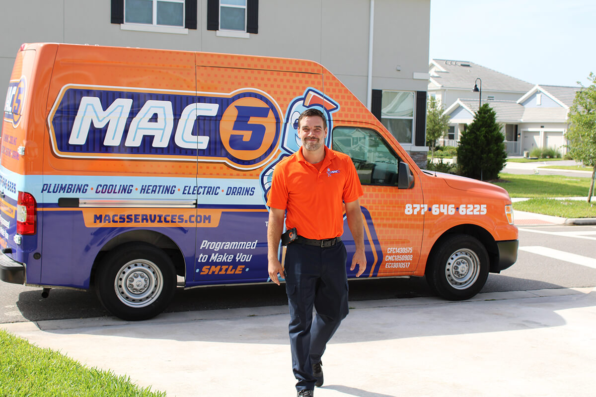 Mac 5 service technicians walking up to a home with a Mac 5 Services van behind him