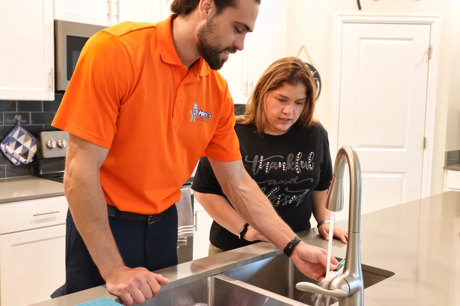 Mac 5 plumber testing faucet water pressure with client.