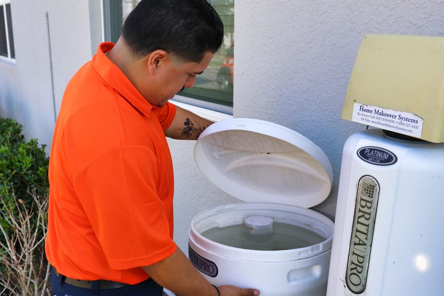 Plumber checking water softening system outside home.